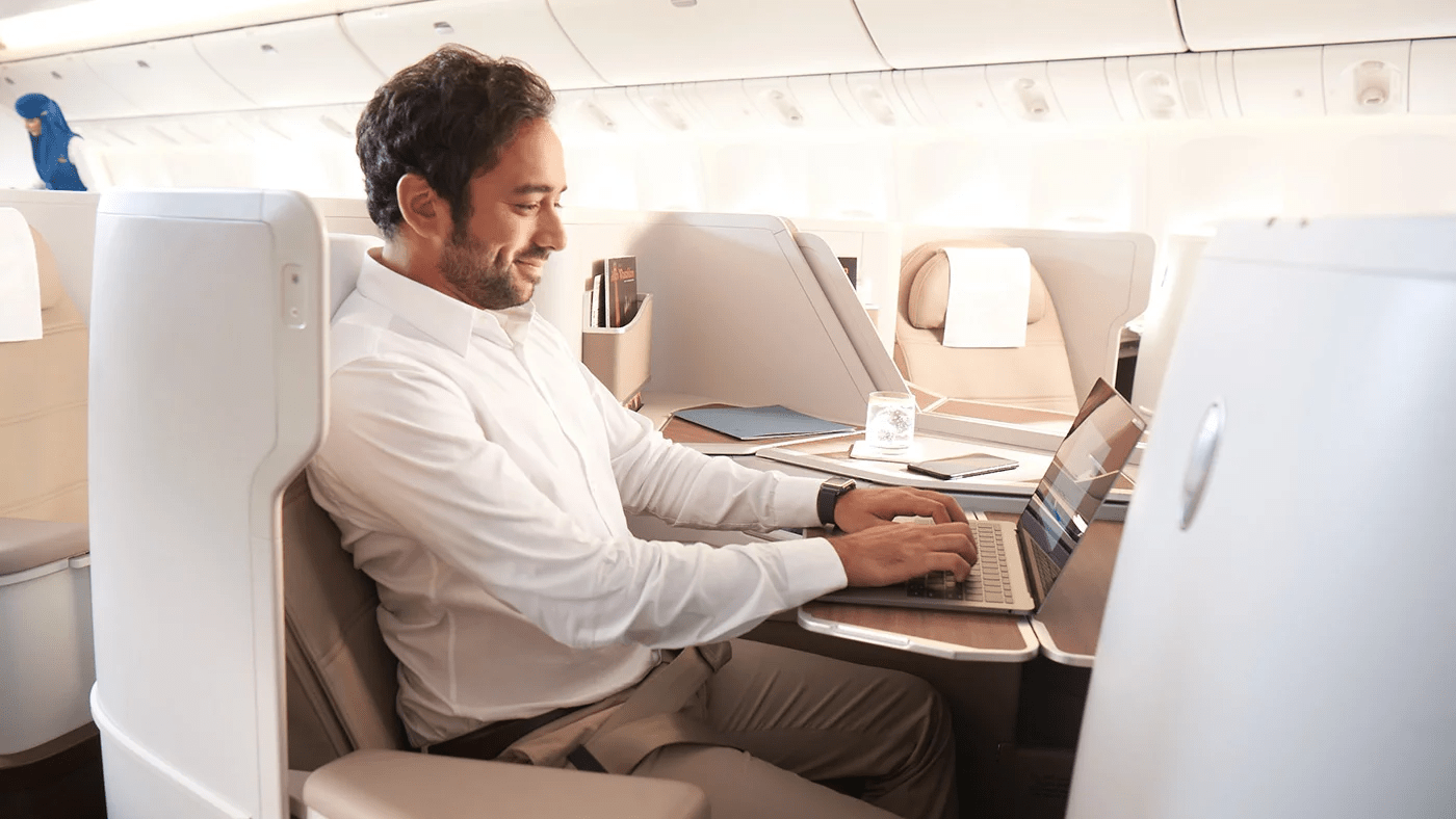 مسافر يجلس مبتسما في درجة الأعمال ويعمل على حاسوبه 